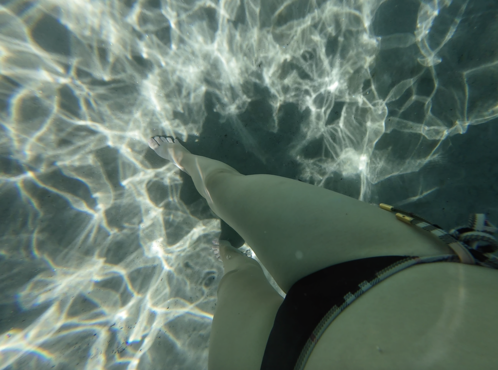 Girl's legs inside the crystal-clear waters of Santa Bábara falls. The ground is white sand.